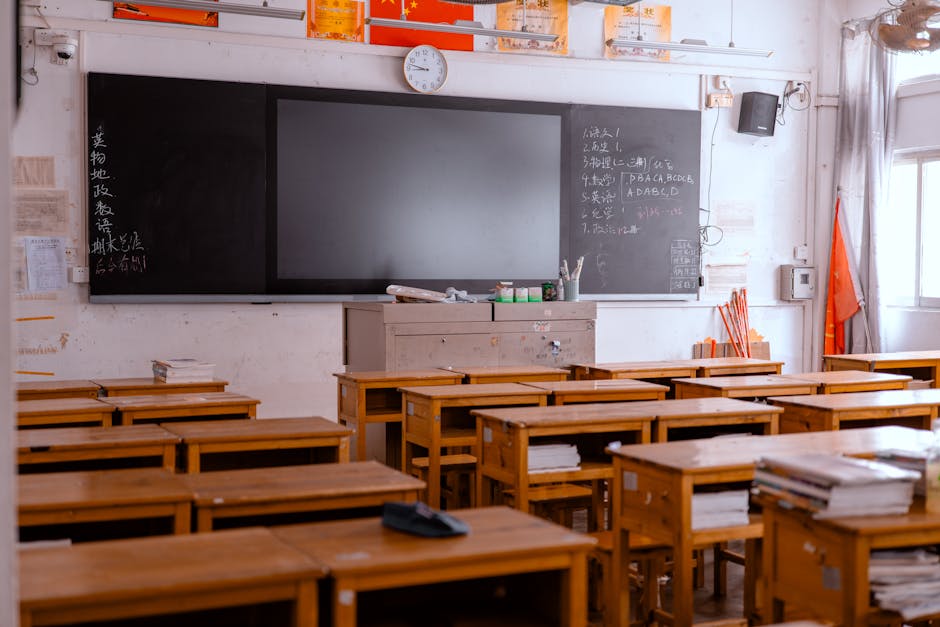 An empty classroom with wooden desks and a blackboard, featuring educational materials.